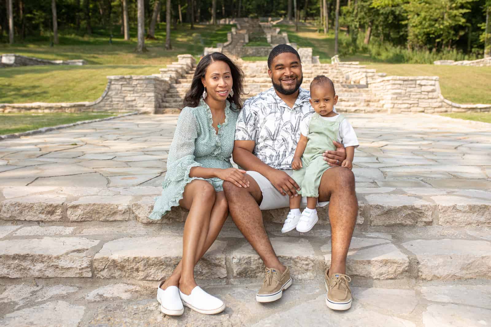 Black couple sitting on steps in park with one year old baby